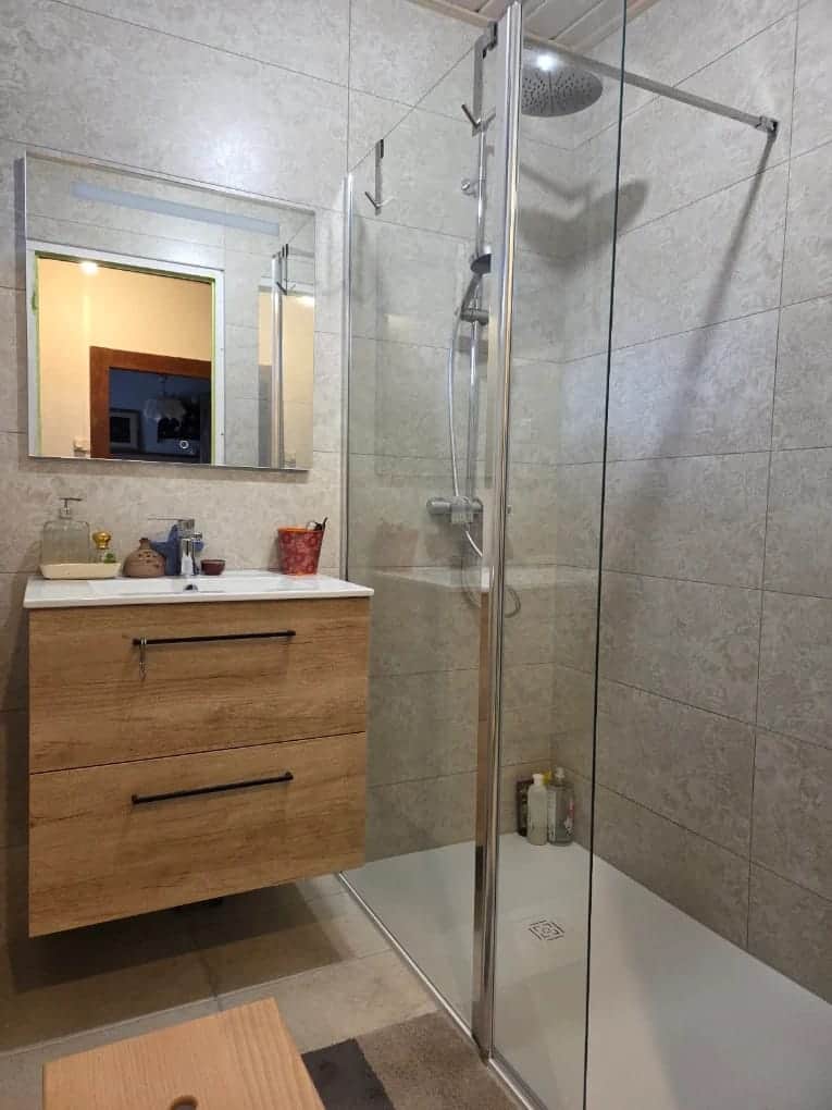 Salle de bain avec douche à paroi vitrée, carrelage beige et meuble vasque en bois, réalisée par AML Plomberie